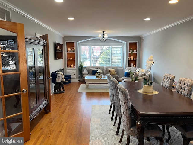 dining space featuring crown molding, a chandelier, built in features, and light hardwood / wood-style floors