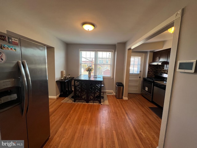 kitchen with dark brown cabinetry, backsplash, stainless steel appliances, and light hardwood / wood-style floors