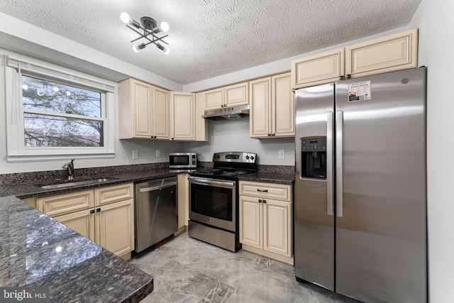 kitchen with appliances with stainless steel finishes, sink, a textured ceiling, and dark stone countertops