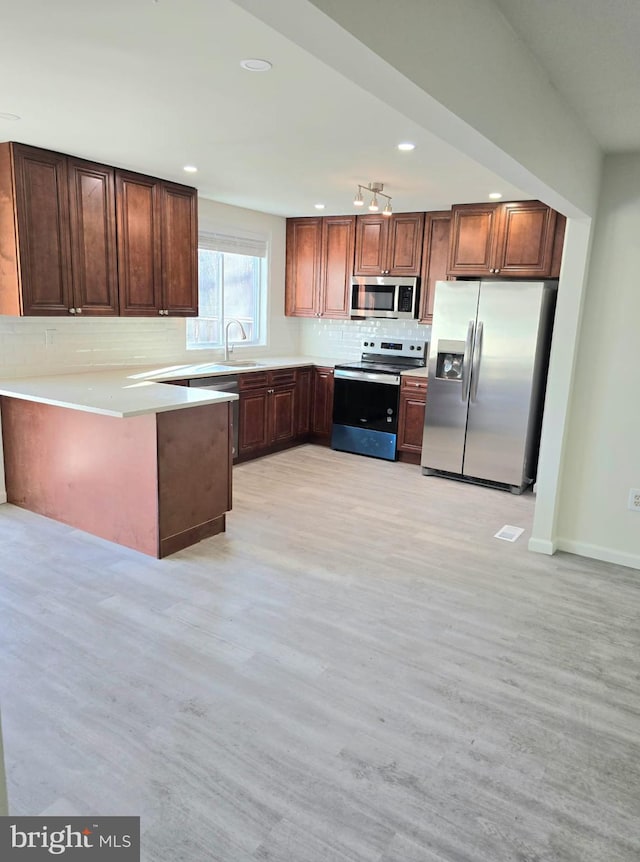 kitchen with sink, tasteful backsplash, light wood-type flooring, appliances with stainless steel finishes, and kitchen peninsula