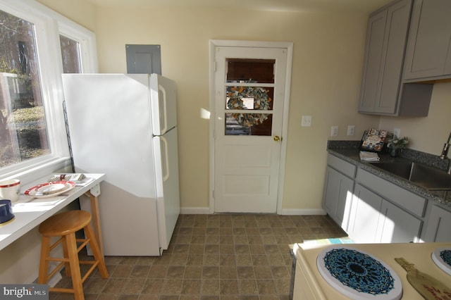 kitchen featuring gray cabinetry, a sink, range, freestanding refrigerator, and dark countertops