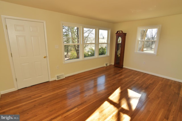 spare room featuring dark wood-style flooring, visible vents, and baseboards