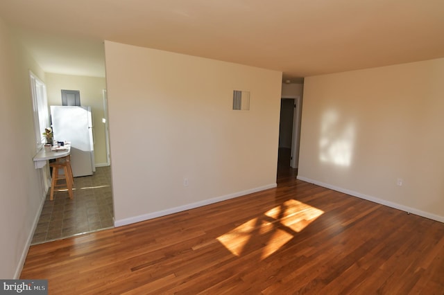 empty room with dark wood-style floors, visible vents, and baseboards