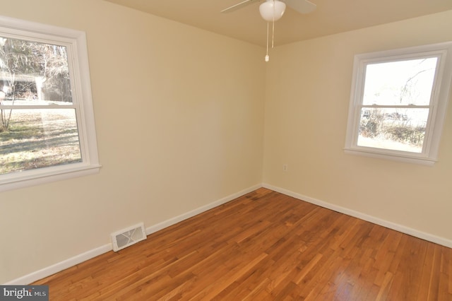 empty room featuring a ceiling fan, wood finished floors, visible vents, and baseboards