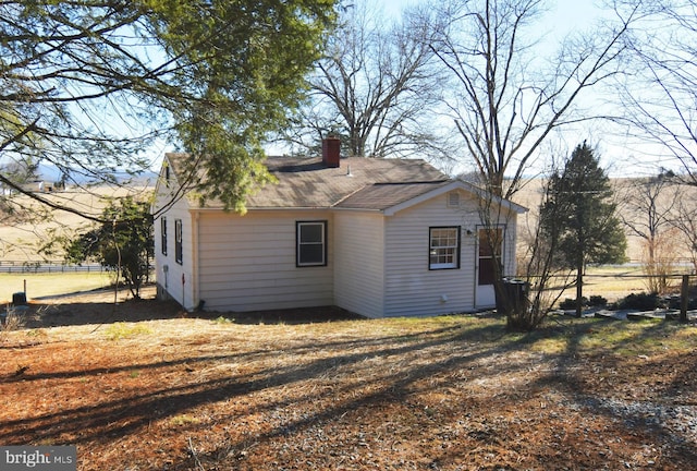 view of side of property featuring a shingled roof, a chimney, and fence