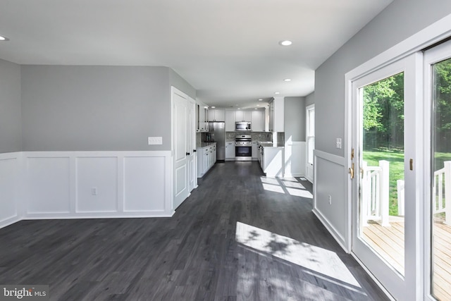 interior space featuring stainless steel appliances, a decorative wall, dark wood-type flooring, wainscoting, and white cabinets