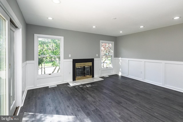 unfurnished living room with wainscoting, dark wood-style flooring, a decorative wall, a glass covered fireplace, and recessed lighting