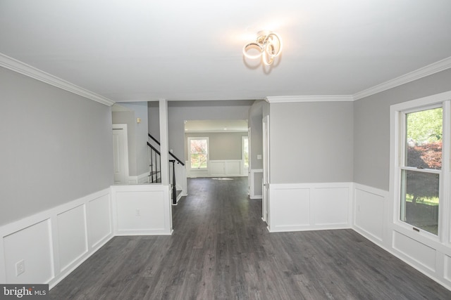empty room featuring a decorative wall, stairway, dark wood finished floors, ornamental molding, and a wainscoted wall