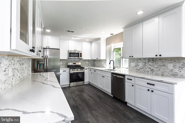 kitchen featuring stainless steel appliances, a sink, white cabinetry, backsplash, and light stone counters