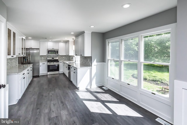 kitchen with appliances with stainless steel finishes, a sink, dark wood-type flooring, backsplash, and white cabinetry