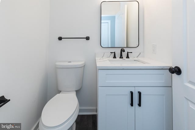 half bath featuring toilet, vanity, and baseboards