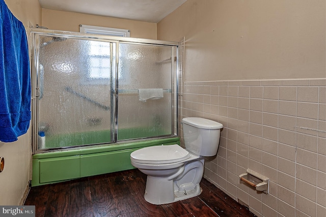 bathroom with hardwood / wood-style floors, toilet, combined bath / shower with glass door, and tile walls