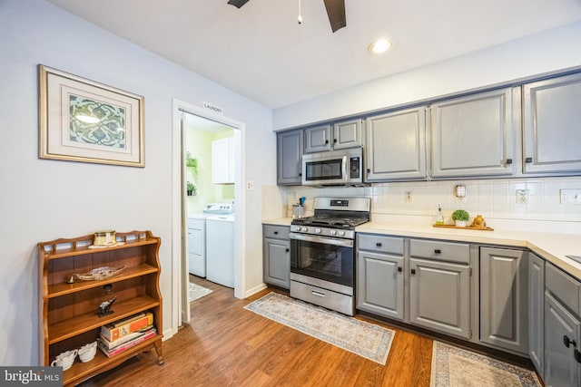 kitchen with light wood-type flooring, gray cabinets, washer and dryer, and appliances with stainless steel finishes