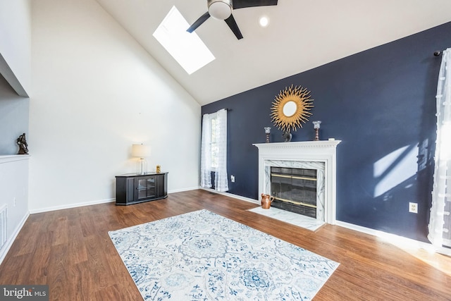 living room with dark hardwood / wood-style floors, high vaulted ceiling, a skylight, ceiling fan, and a high end fireplace