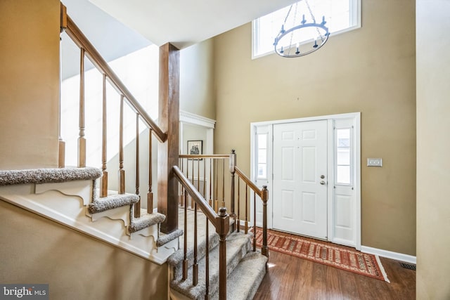 entrance foyer with hardwood / wood-style flooring, a towering ceiling, and a notable chandelier