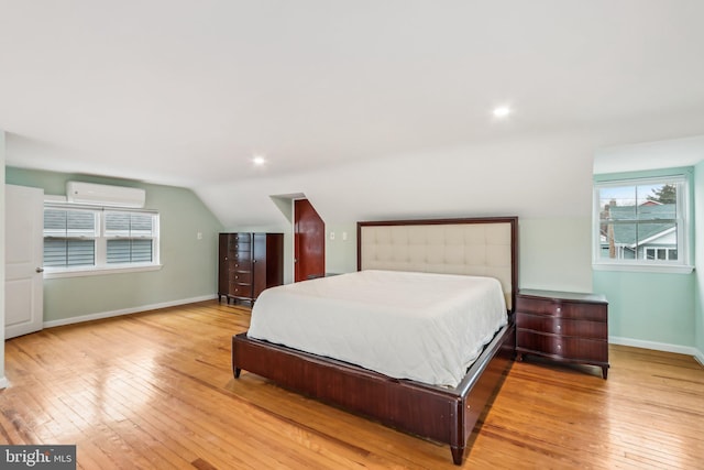 bedroom featuring lofted ceiling, light hardwood / wood-style flooring, and a wall unit AC