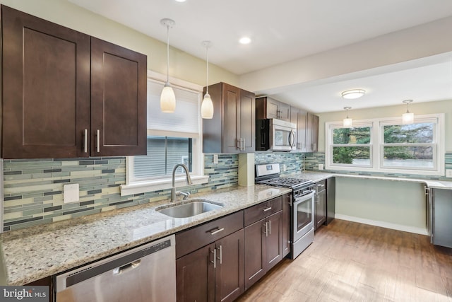 kitchen with light stone counters, hanging light fixtures, sink, and appliances with stainless steel finishes