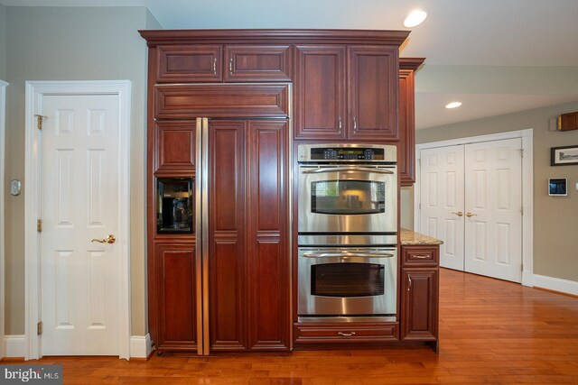 kitchen with light stone countertops, double oven, wood finished floors, and recessed lighting