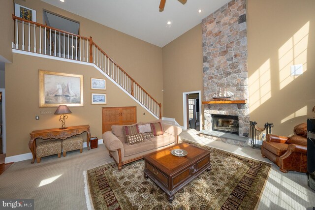 living room featuring light colored carpet, a fireplace, a towering ceiling, baseboards, and stairway