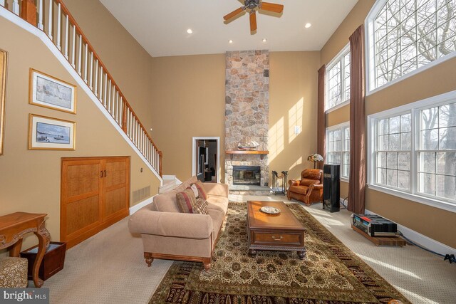 living room featuring stairway, light colored carpet, a fireplace, and a towering ceiling