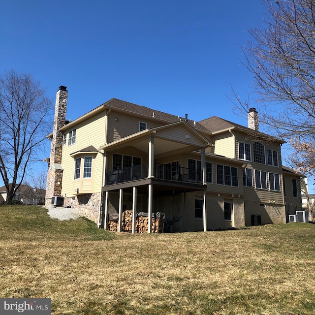 rear view of house with a chimney, cooling unit, and a yard