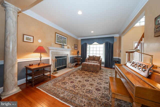 sitting room with ornamental molding, wainscoting, a tile fireplace, and ornate columns