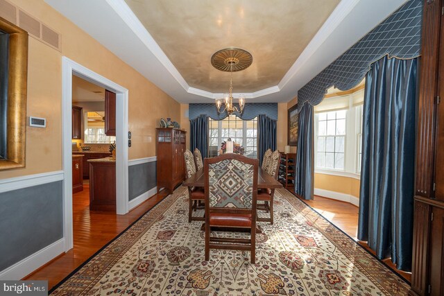 dining area featuring a raised ceiling, visible vents, a notable chandelier, and light wood finished floors