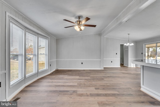 unfurnished living room with ceiling fan with notable chandelier, ornamental molding, and light hardwood / wood-style floors