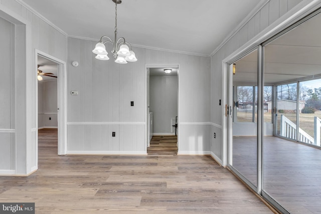 unfurnished dining area featuring crown molding, ceiling fan with notable chandelier, and light wood-type flooring