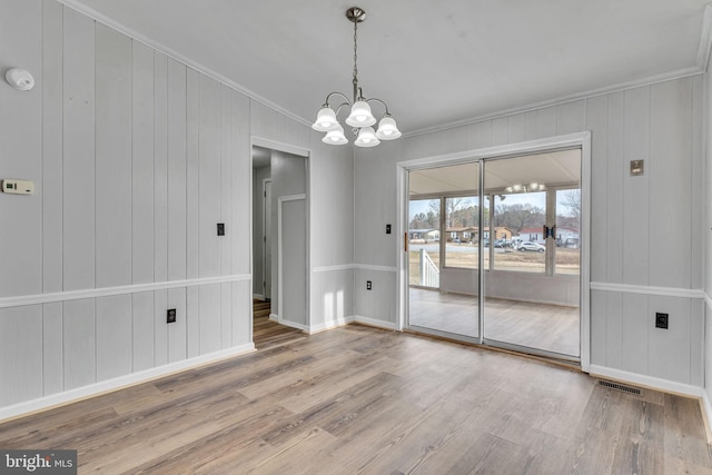 empty room featuring wood-type flooring, a notable chandelier, and crown molding