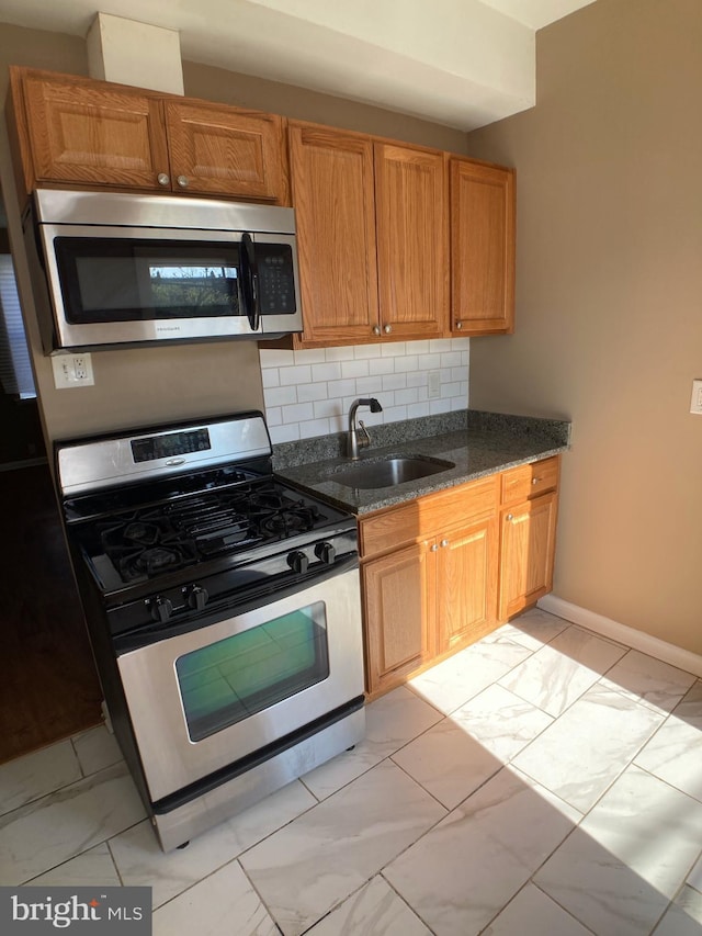 kitchen featuring stainless steel appliances, sink, decorative backsplash, and dark stone countertops