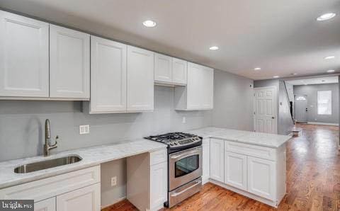 kitchen featuring white cabinetry, sink, kitchen peninsula, stainless steel gas range, and light wood-type flooring