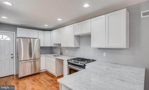 kitchen featuring sink, appliances with stainless steel finishes, white cabinetry, backsplash, and light wood-type flooring