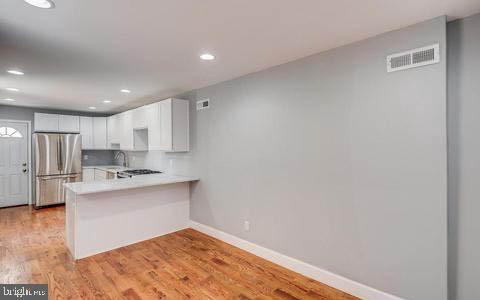 kitchen featuring sink, white cabinets, stainless steel fridge, light hardwood / wood-style floors, and kitchen peninsula