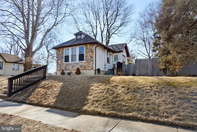 view of front of home featuring stone siding, a front lawn, and fence