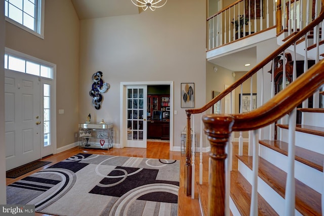 foyer featuring baseboards, stairs, a towering ceiling, and light wood-style floors