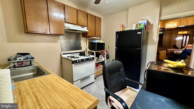 kitchen featuring light countertops, freestanding refrigerator, a sink, under cabinet range hood, and white gas range oven