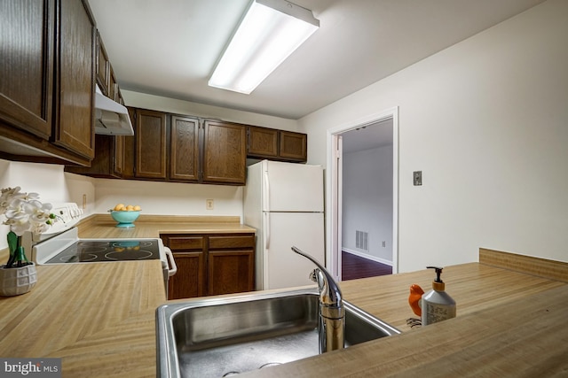 kitchen featuring dark brown cabinetry, under cabinet range hood, white appliances, a sink, and light countertops