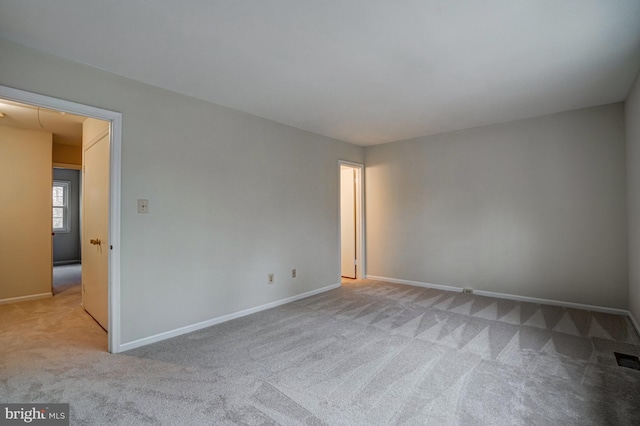 spare room featuring light carpet and baseboards