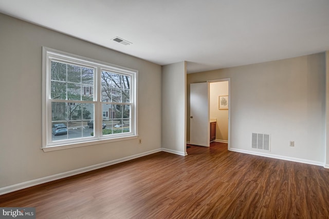 empty room with wood finished floors, visible vents, and baseboards