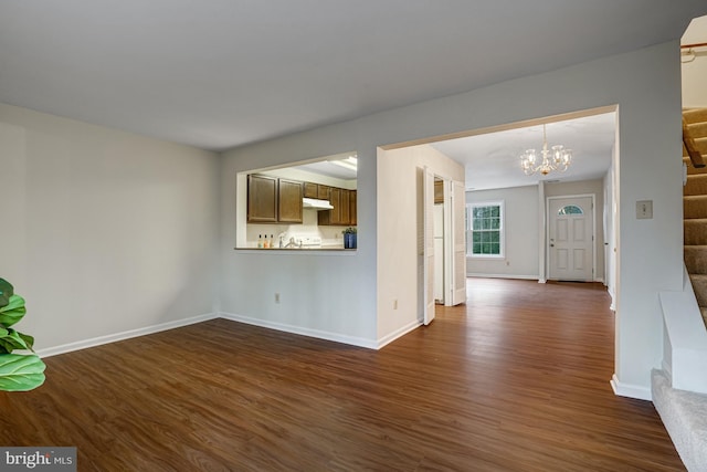 unfurnished living room featuring stairs, dark wood-type flooring, a notable chandelier, and baseboards