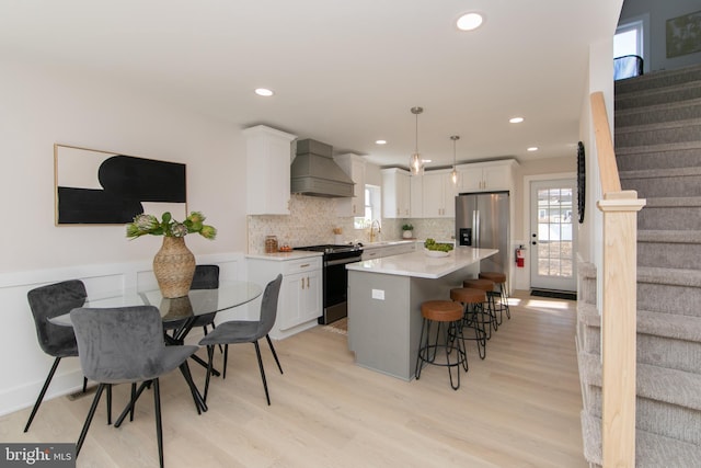 kitchen with pendant lighting, white cabinetry, a center island, stainless steel appliances, and custom range hood