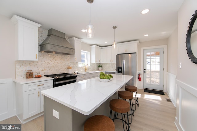 kitchen featuring gas stove, stainless steel fridge, a kitchen island, custom range hood, and white cabinets