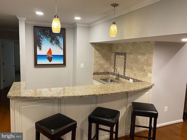 bar featuring sink, light stone countertops, hanging light fixtures, and a kitchen bar