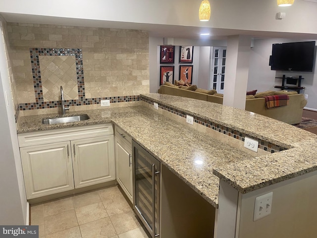 kitchen featuring sink, beverage cooler, light stone counters, and decorative backsplash