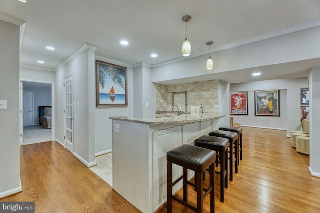 kitchen featuring a kitchen bar, crown molding, decorative light fixtures, light hardwood / wood-style flooring, and light stone countertops