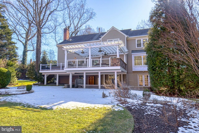 snow covered rear of property with a balcony, a pergola, and a lawn