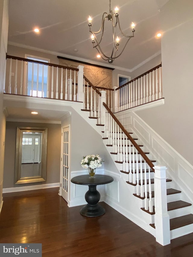 stairs with an inviting chandelier, crown molding, a high ceiling, and hardwood / wood-style flooring