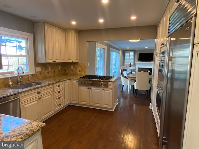 kitchen featuring dark hardwood / wood-style floors, sink, decorative backsplash, stainless steel appliances, and light stone countertops