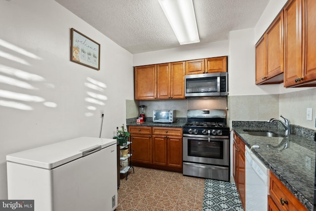 kitchen with stainless steel appliances, sink, dark stone countertops, and a textured ceiling